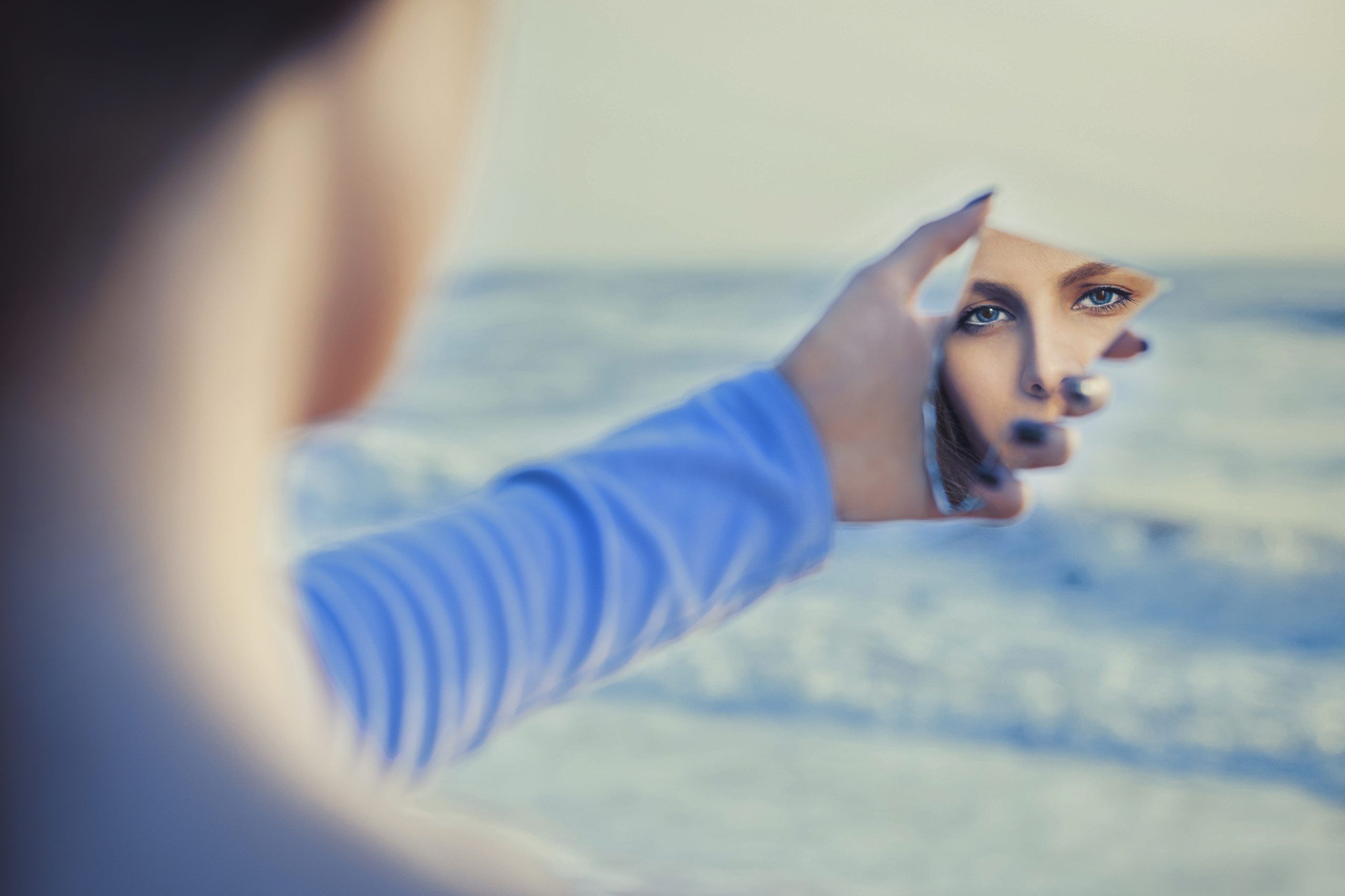 femme à la mer qui tient un morceau de miroir dans la main et voit son reflet